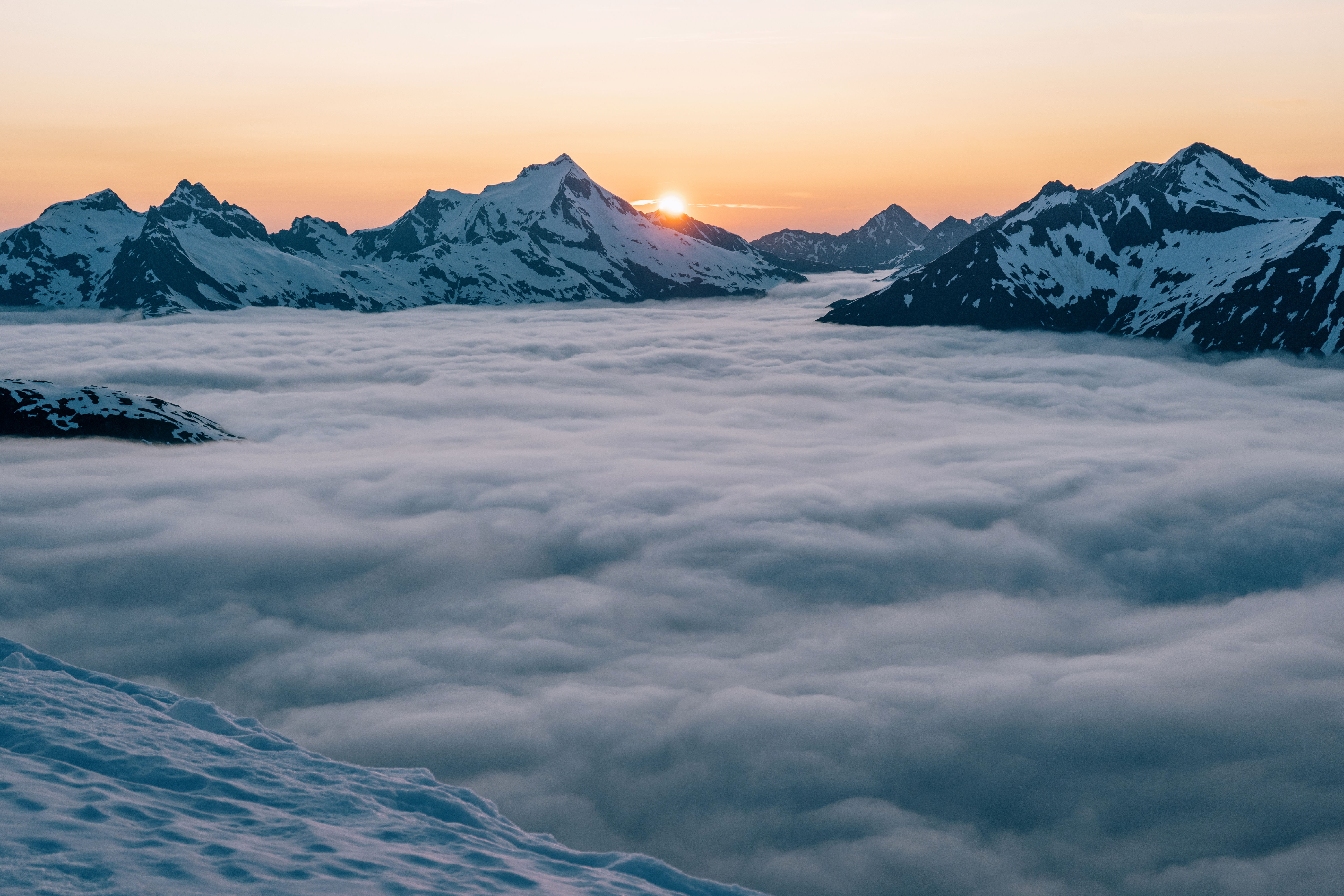 Sunrise over snow-covered mountains above a sea of clouds.