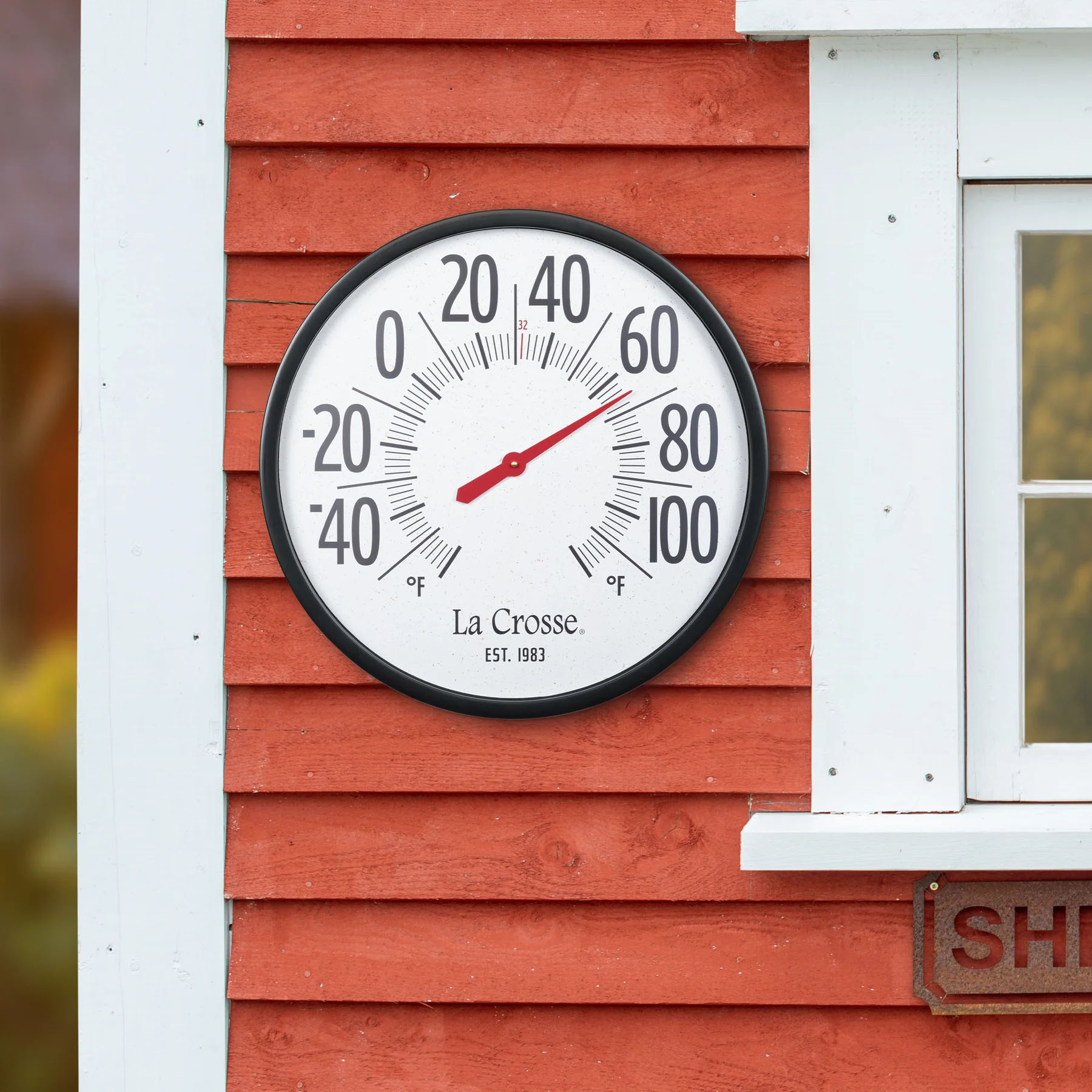104-3056 thermometer on a red wooden wall showing temperature readings.
