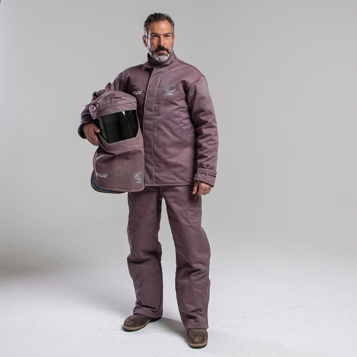 Man in protective clothing holding a helmet, standing against a plain backdrop.