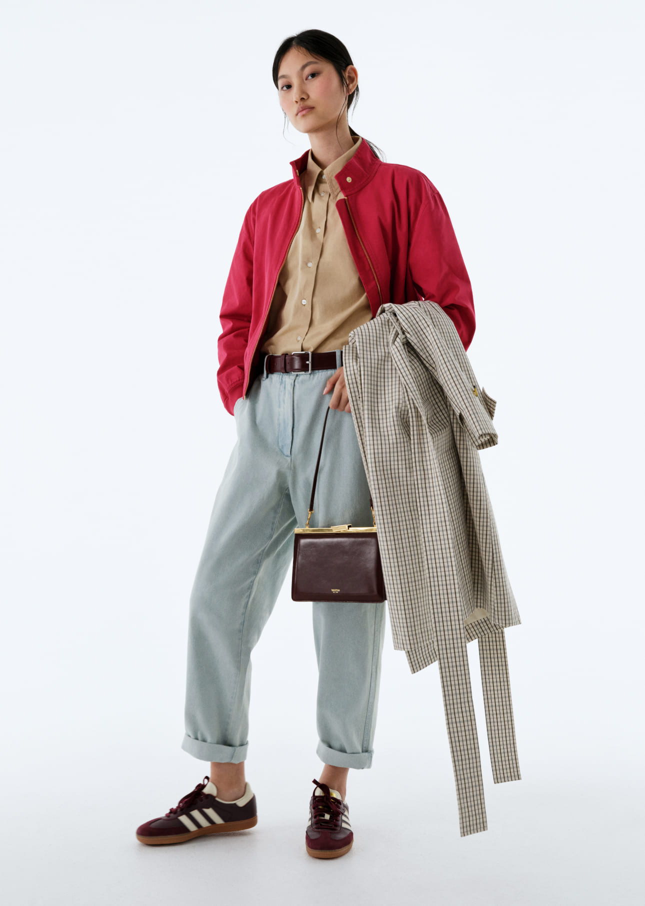A person wearing a red jacket, beige shirt, and light blue pants, holding a coat.