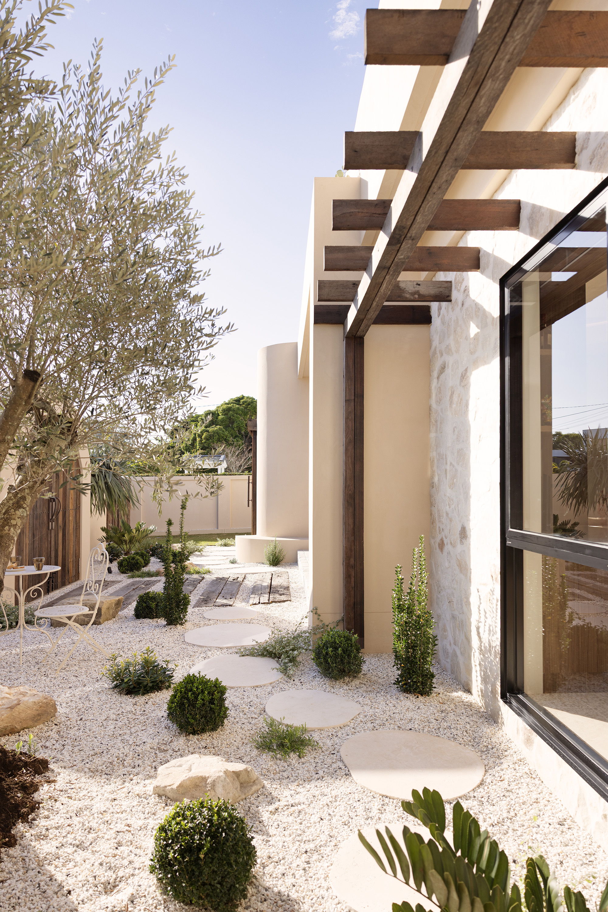 Modern architecture with garden, stone pathways, and greenery under a clear sky.