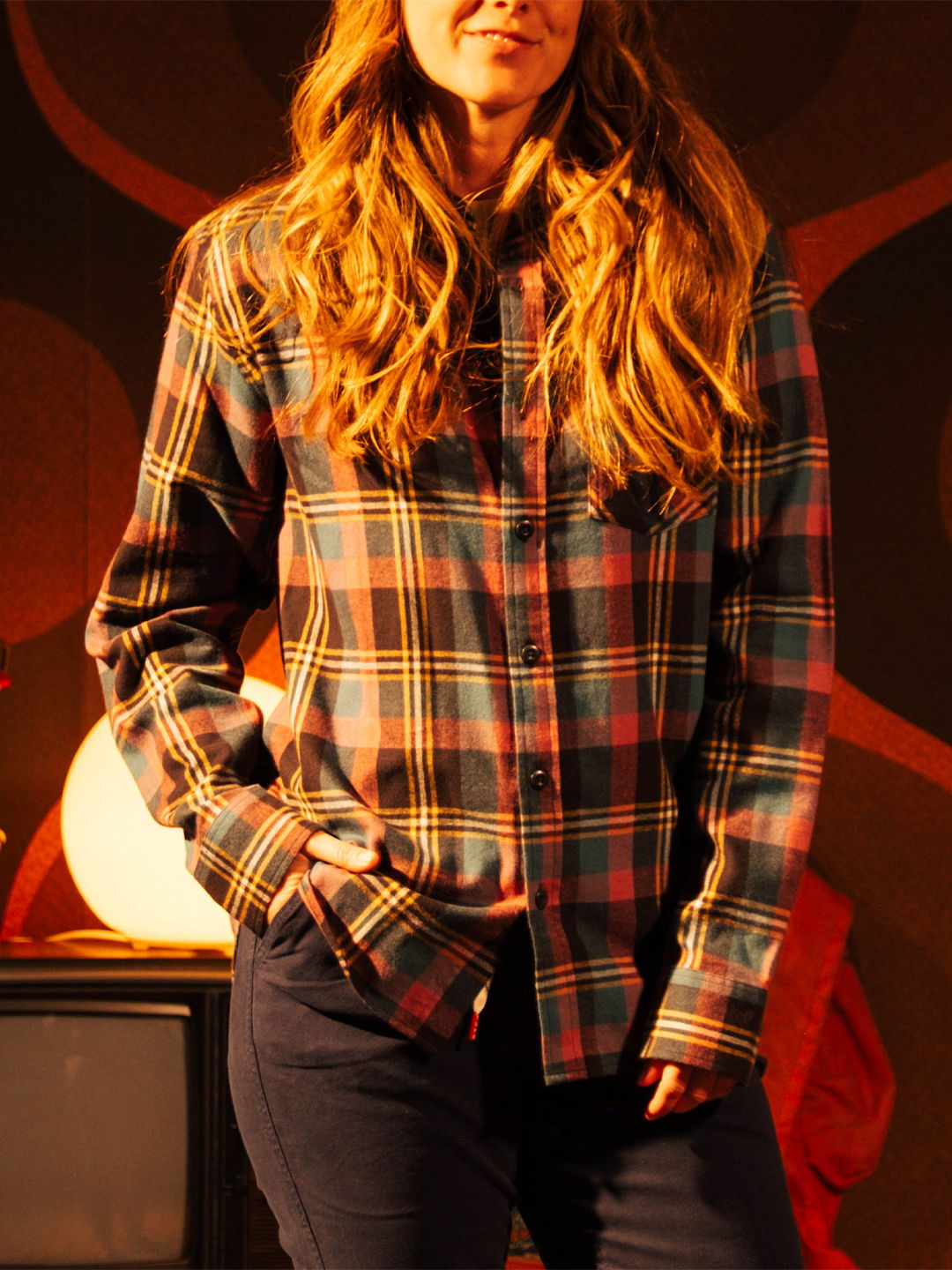 Woman wearing a plaid shirt, standing with hands in pockets.