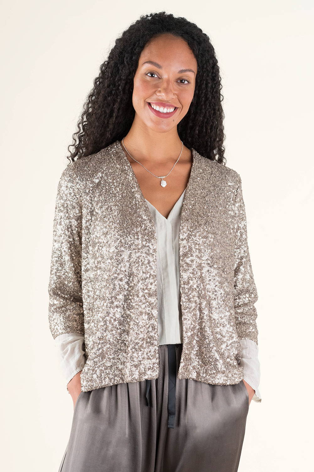 A model wearing a champagne cold sparkly jacket with a pearl necklace