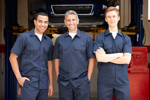 Three mechanics posing together in a garage setting.
