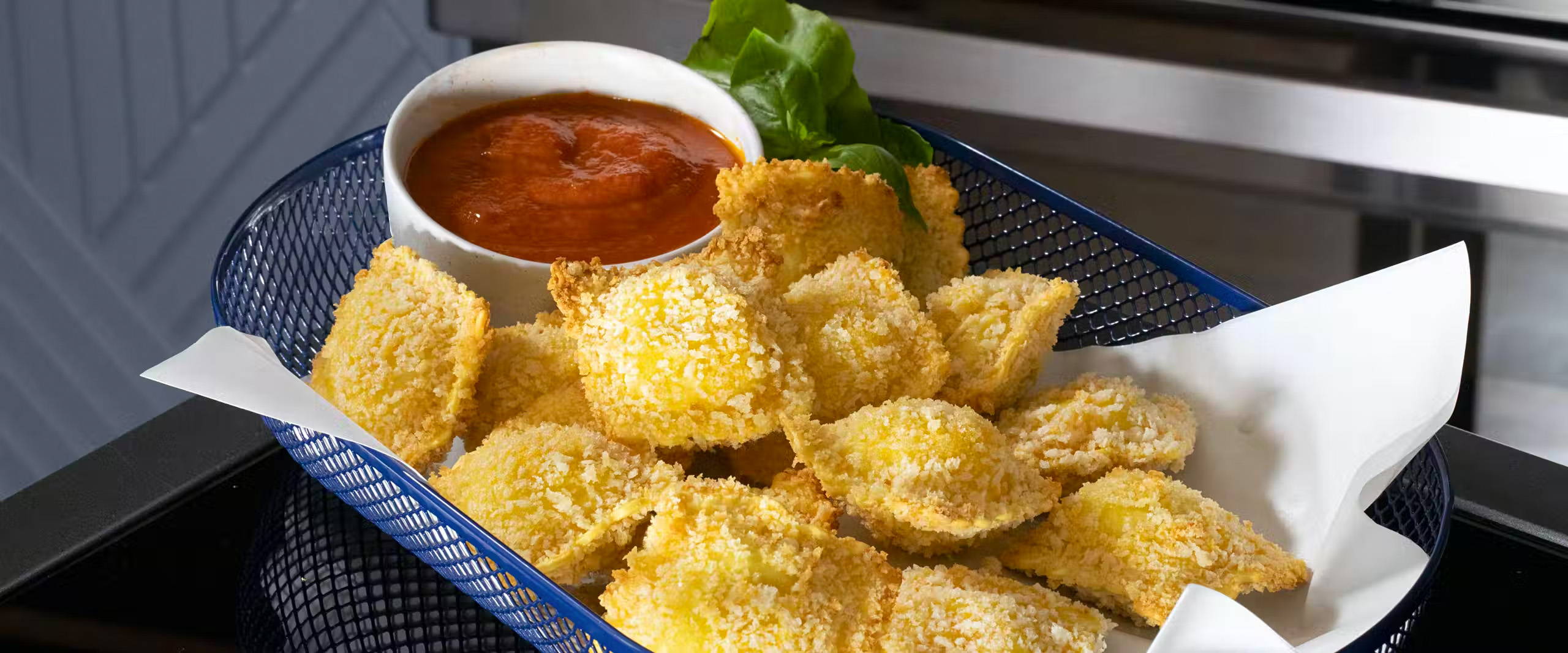 Fried ravioli in a basket with a side of dipping sauce