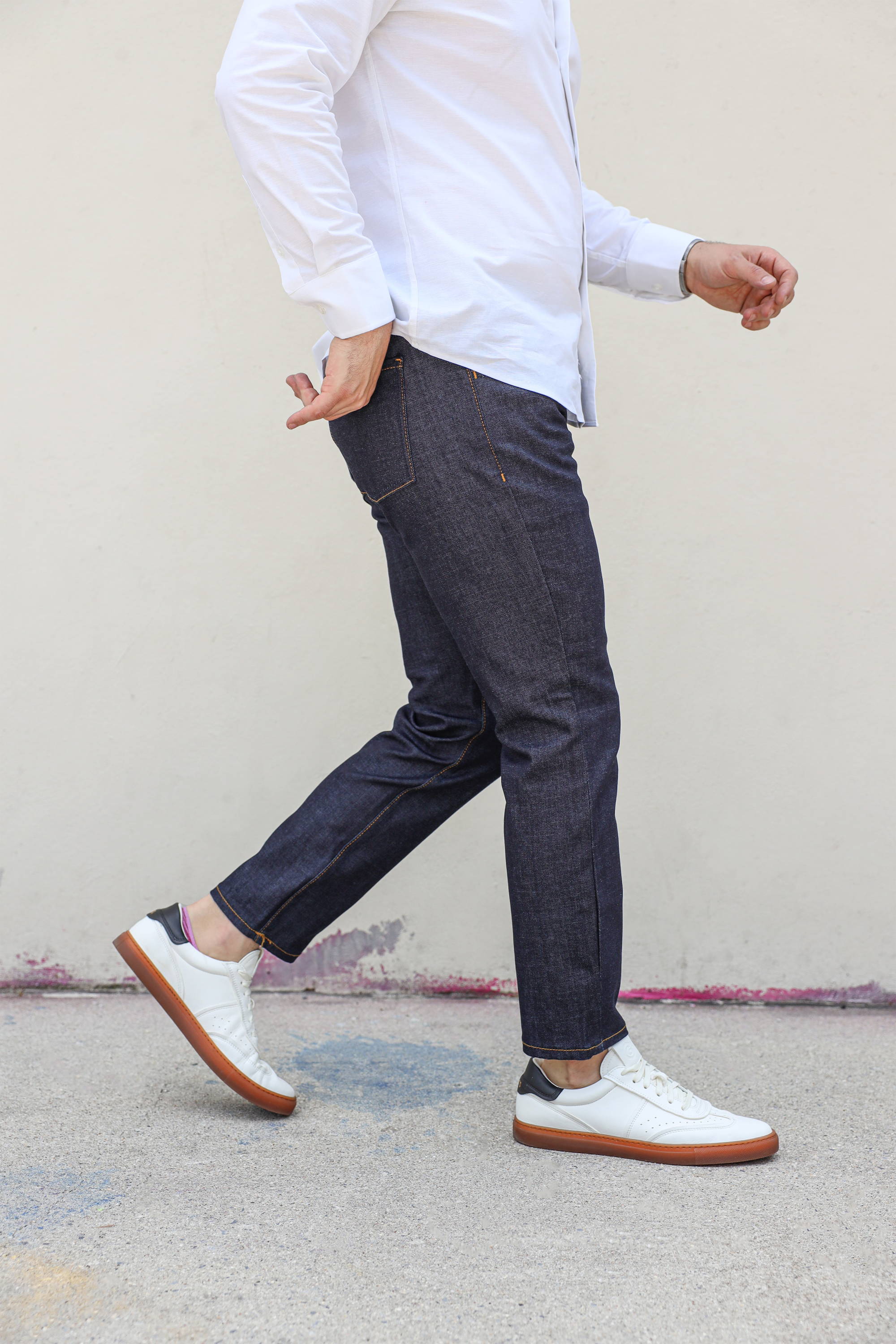 Man walking wearing white tennis shoes, white button down shirt, and Xavier Raw Wash Stretch Jeans from Under510.com