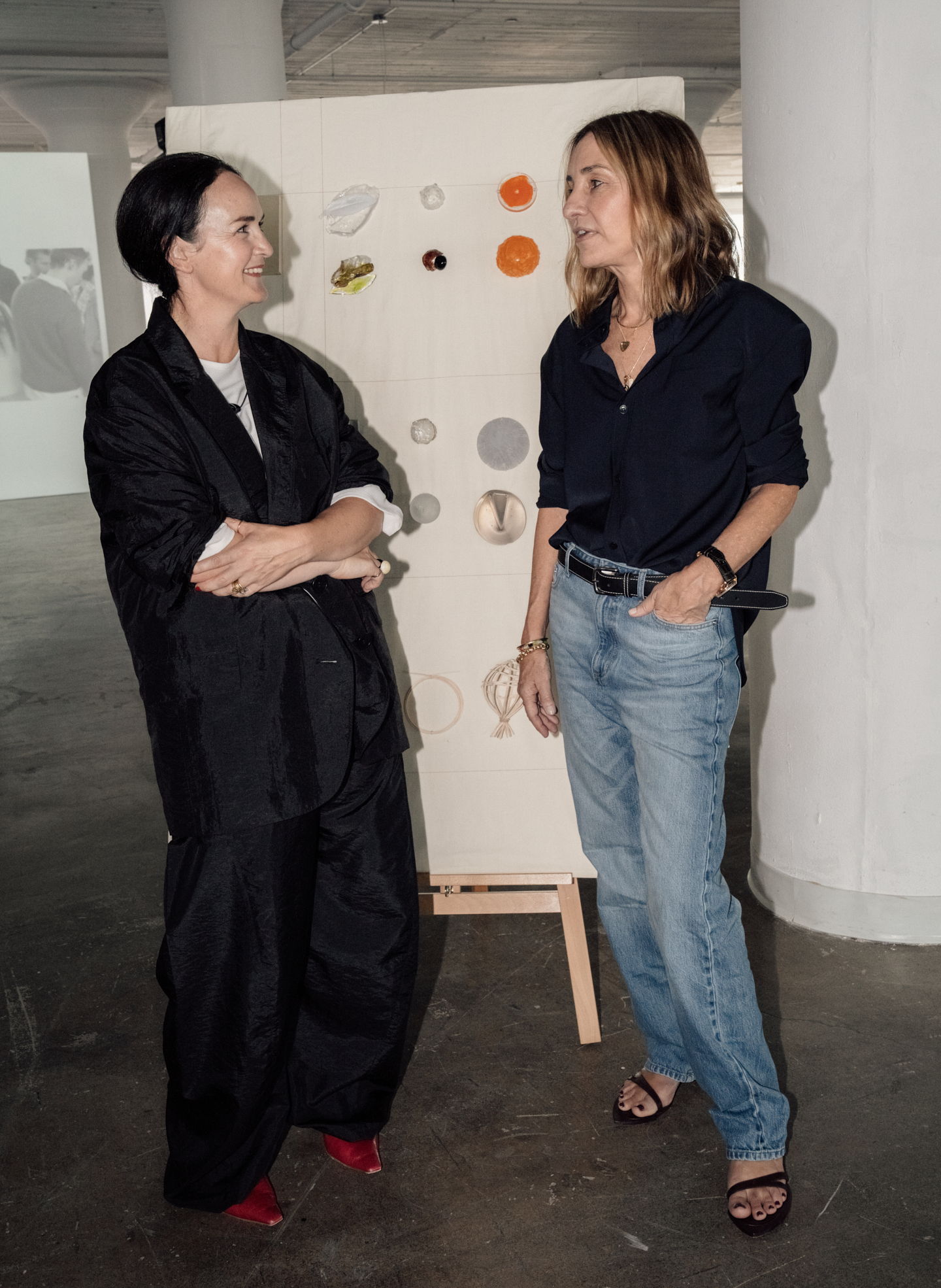 Two women talking in an art gallery, with a display of circles behind them.
