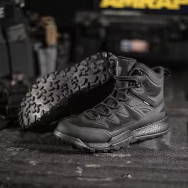 Black tactical boots displayed on a dark surface with equipment in background.