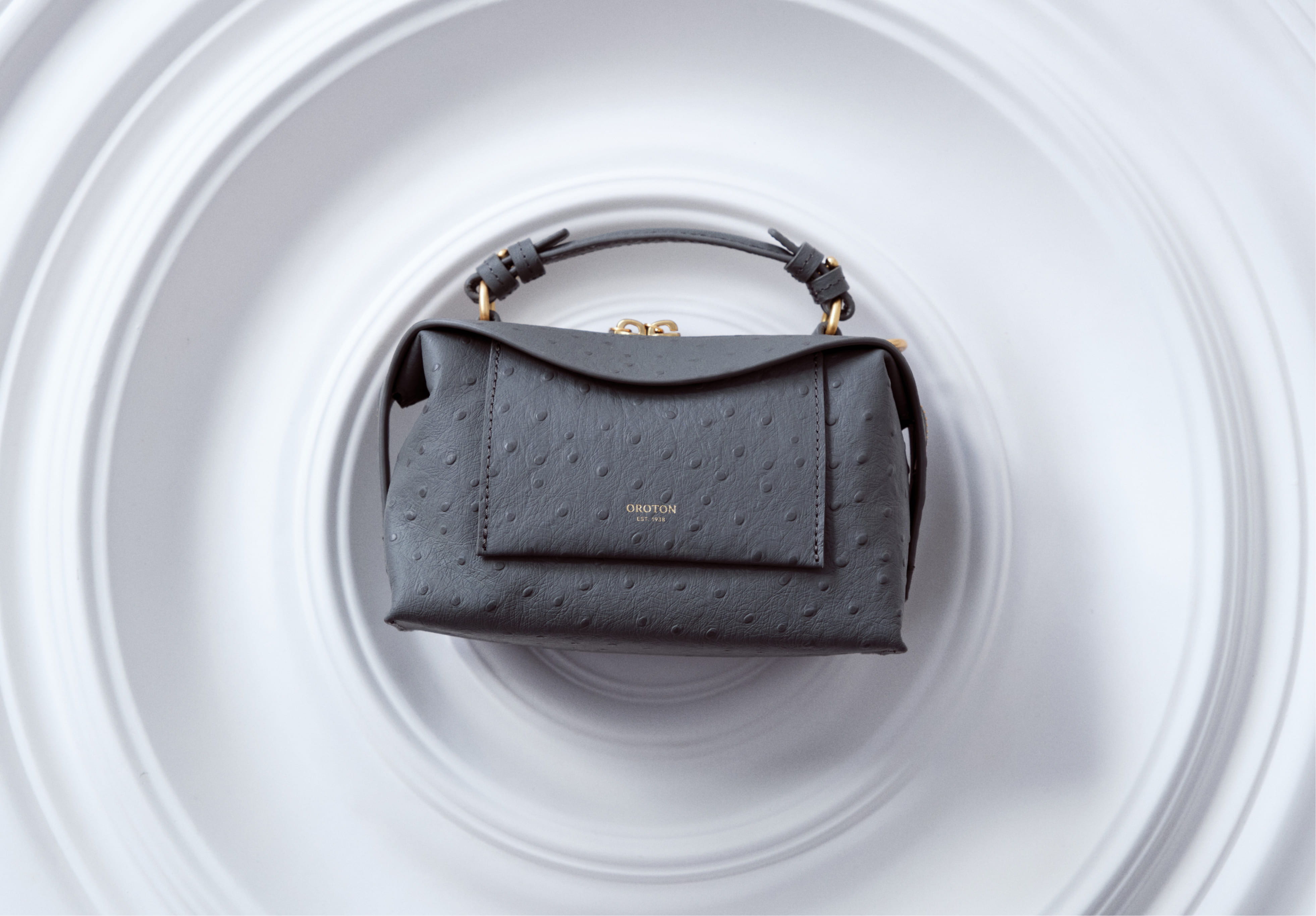 A stylish black handbag displayed on a circular white background.