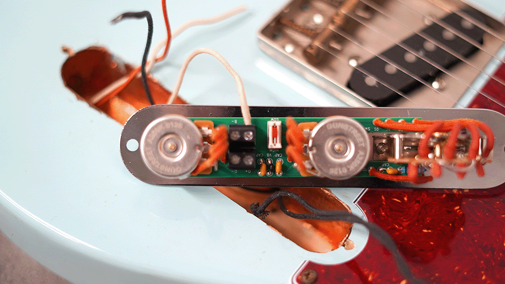 Guitar pickup assembly with wires and circuit board on a light blue guitar body.