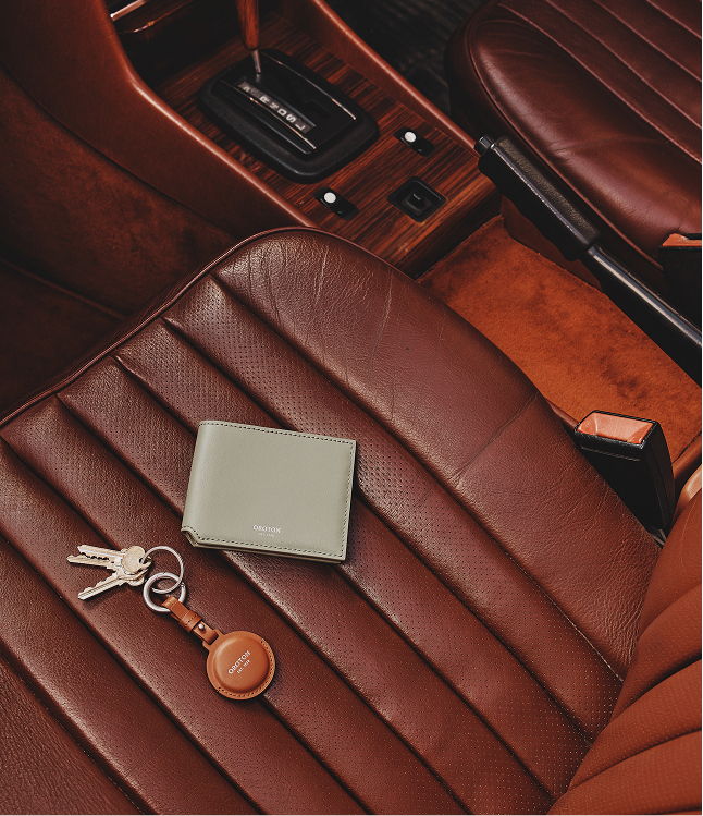 A wallet and keys on a brown leather car seat.