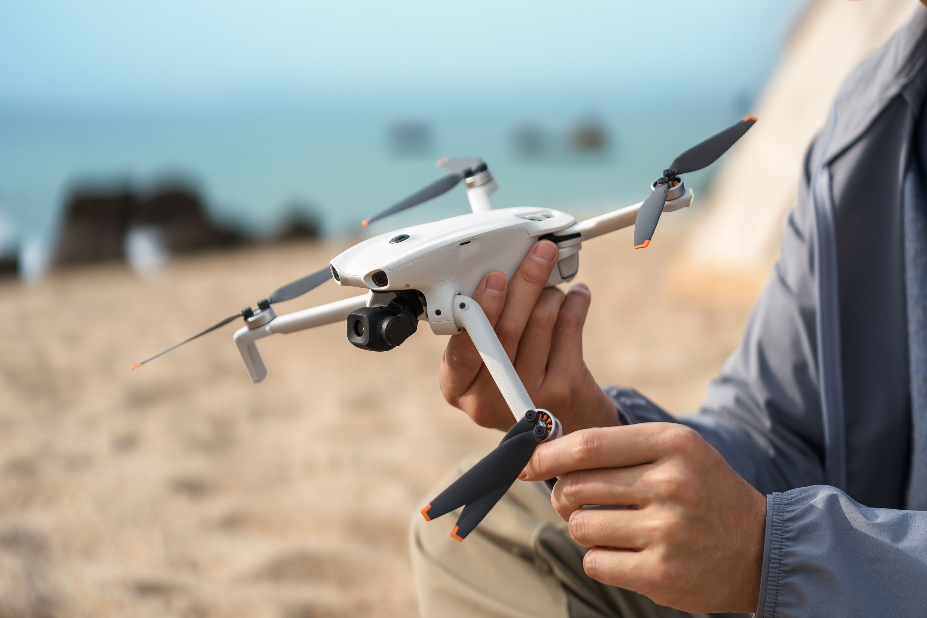Person holding a DJI Lito 1 drone on a beach with ocean in the background.