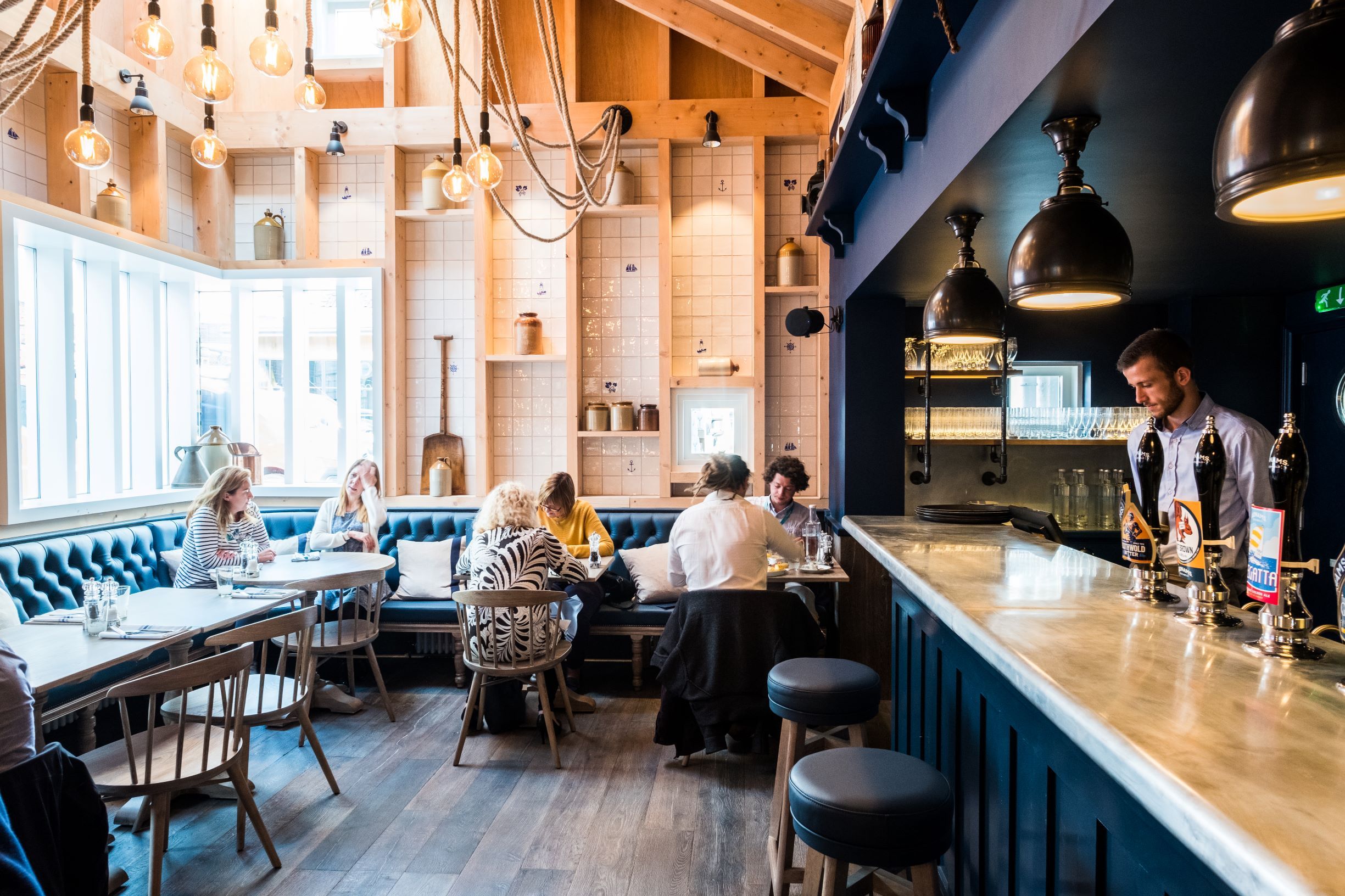 Modern restaurant interior with customers, bar, and wooden decor.