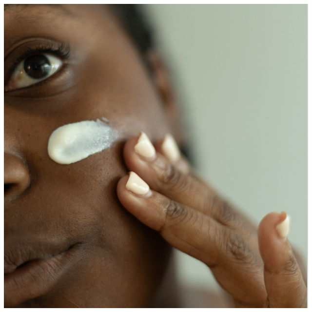 A woman applying a cream to her left cheek
