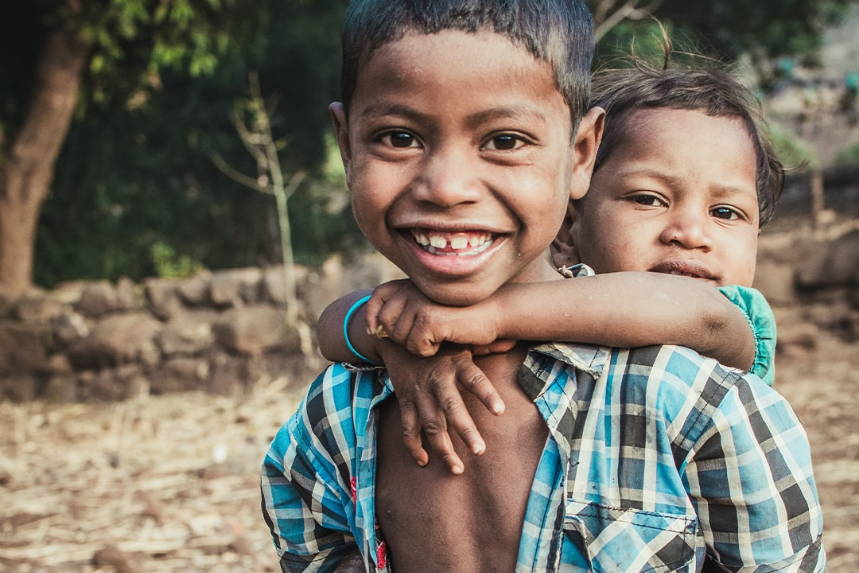 Two children smiling outdoors, one with an arm around the other