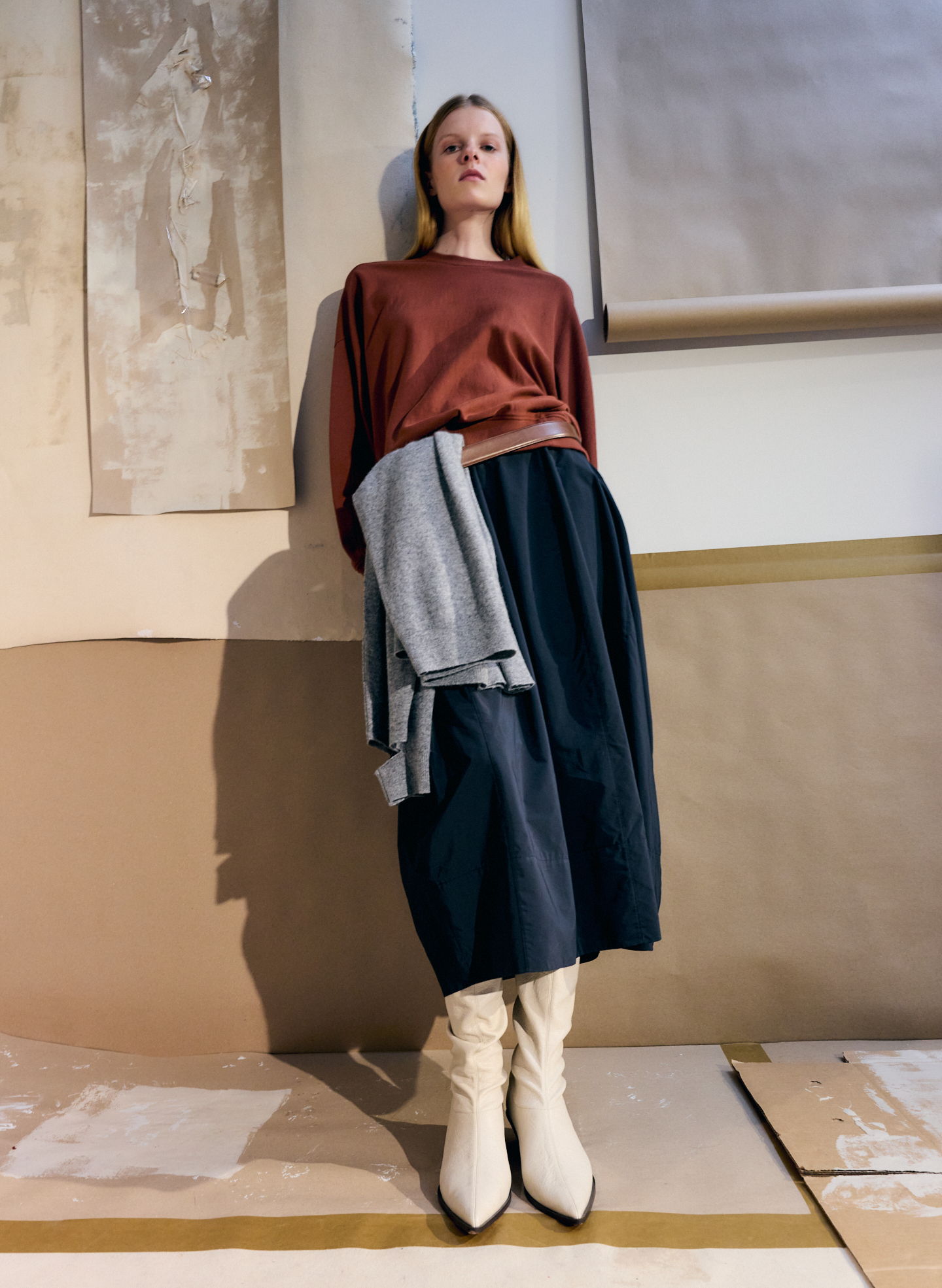 Model wearing a brown top, black skirt, and white boots in a studio setting.