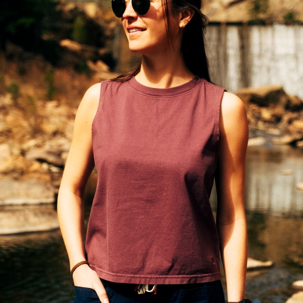 Young woman in sunglasses, wearing a sleeveless top near a waterfall.