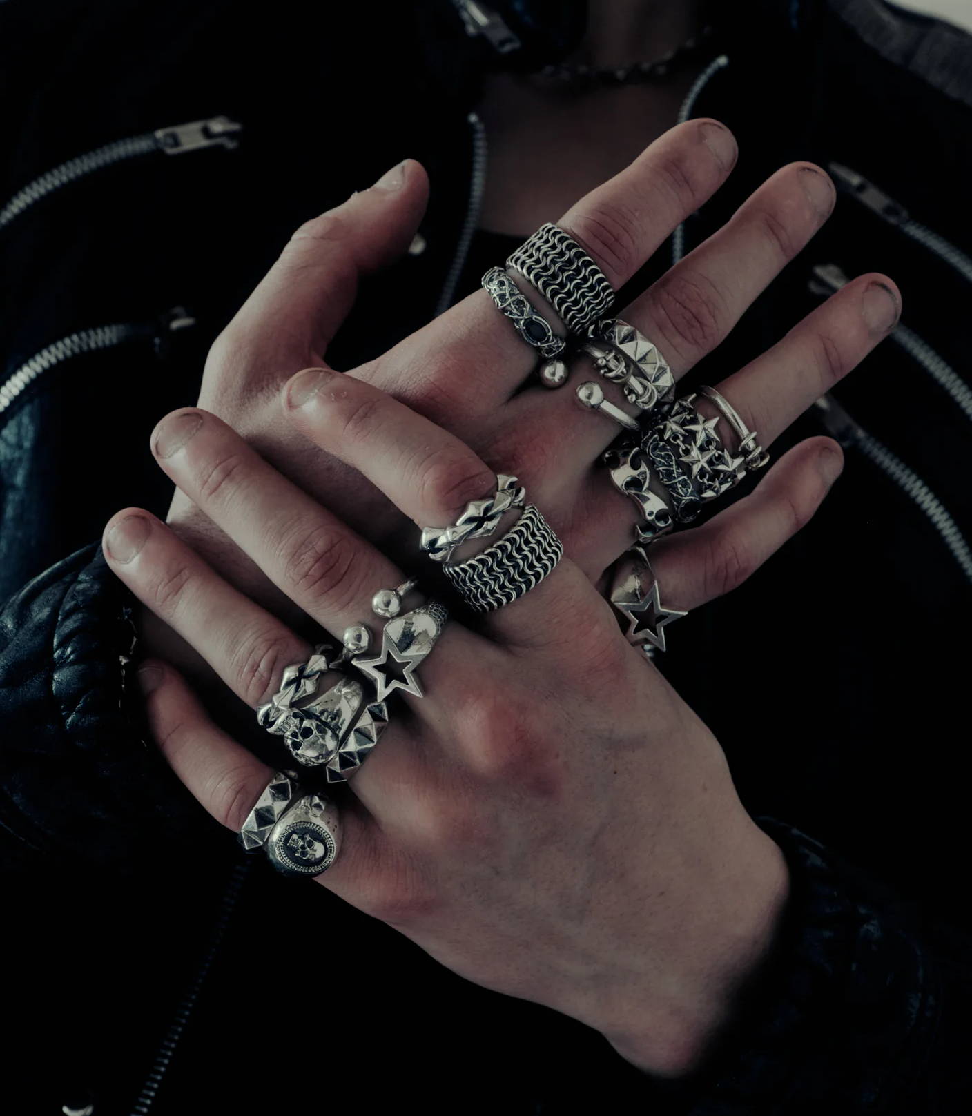 Hands adorned with multiple silver rings, wearing a black leather jacket.