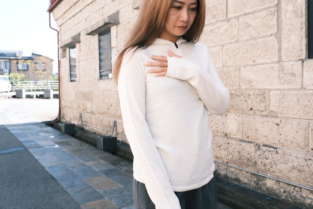 A woman in a white long-sleeve shirt stands on a street.