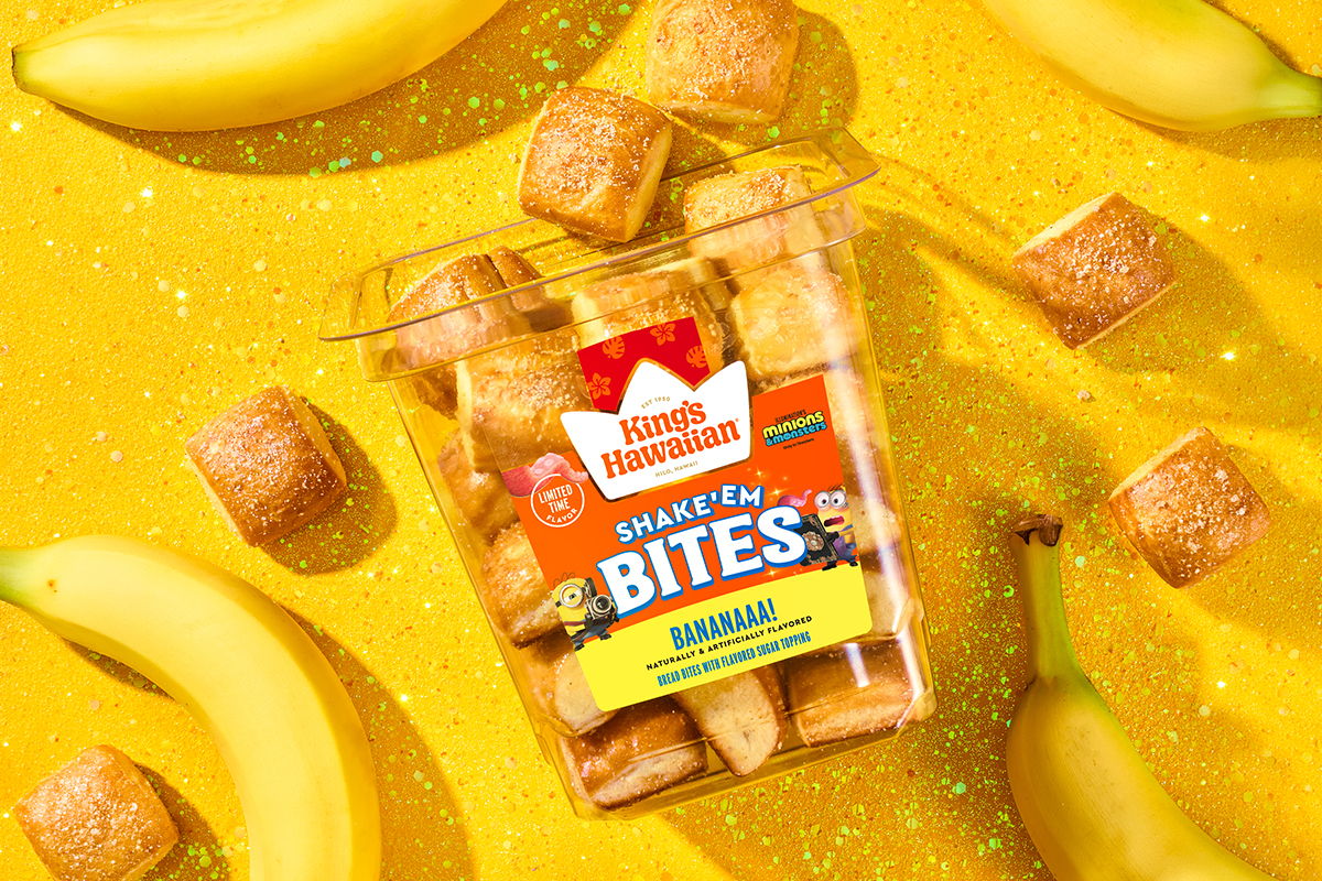 Tub of Shake 'Em Bananaaa! Bites surrounded by bananas on a bright yellow background.