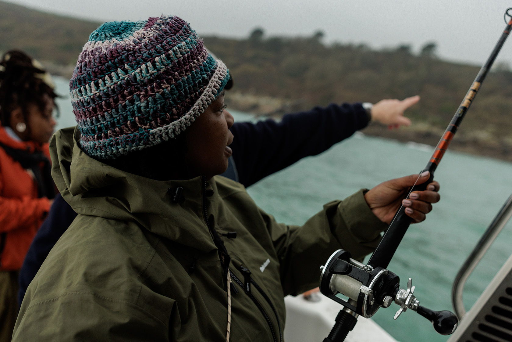 Person fishing on a boat, with another pointing towards the shore.