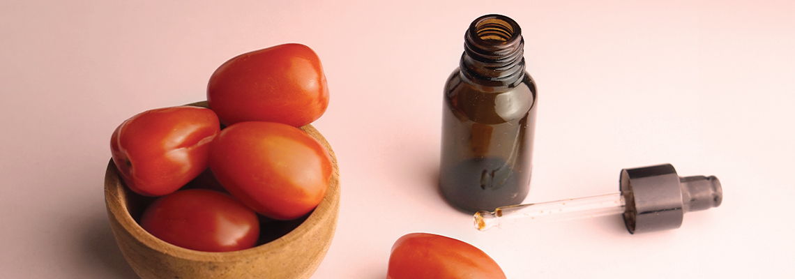 Bowl of tomatoes next to a dropper bottle on a pink background.