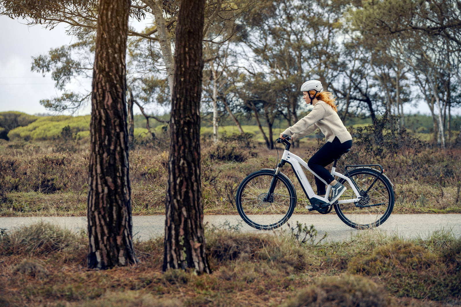 A woman rides a Riese & Muller Charger e-bike along a forest path.