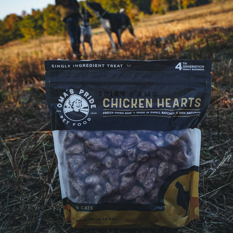 Oma's Pride freeze-dried chicken hearts  in field with dogs behind.