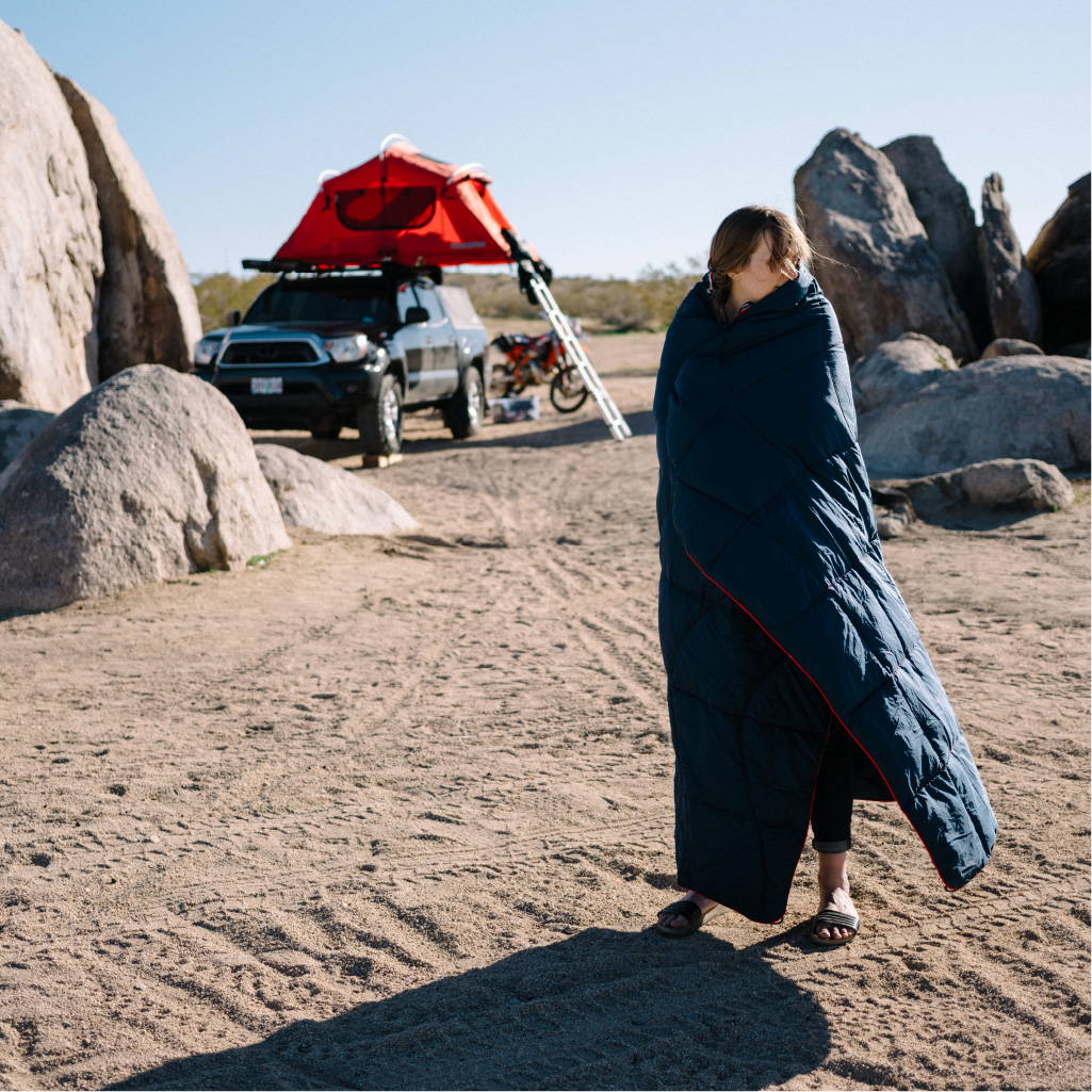 Woman wrapped in blue blanket outside her Toyota Tacoma truck and tent