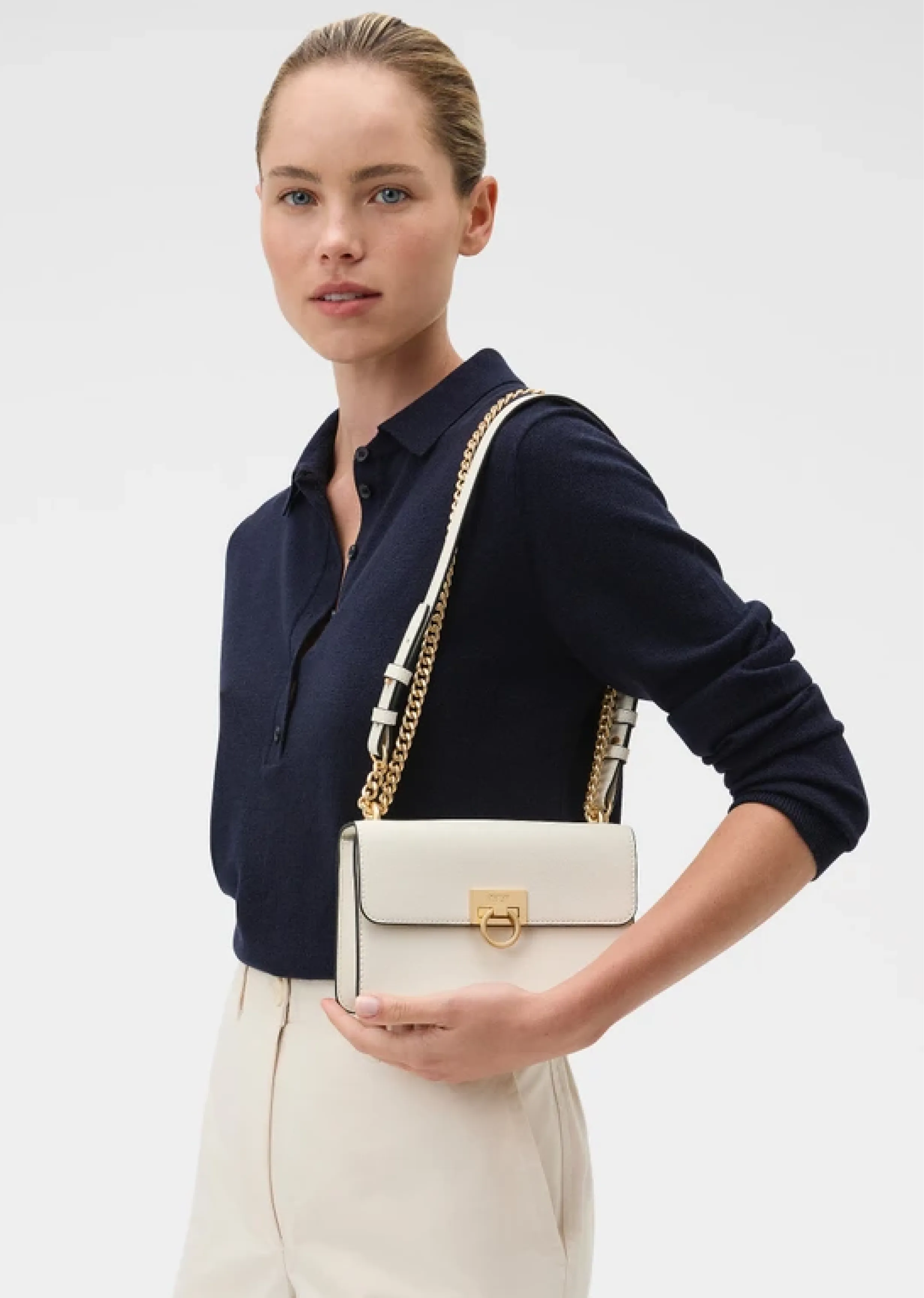 A woman in a navy top holding a white handbag.