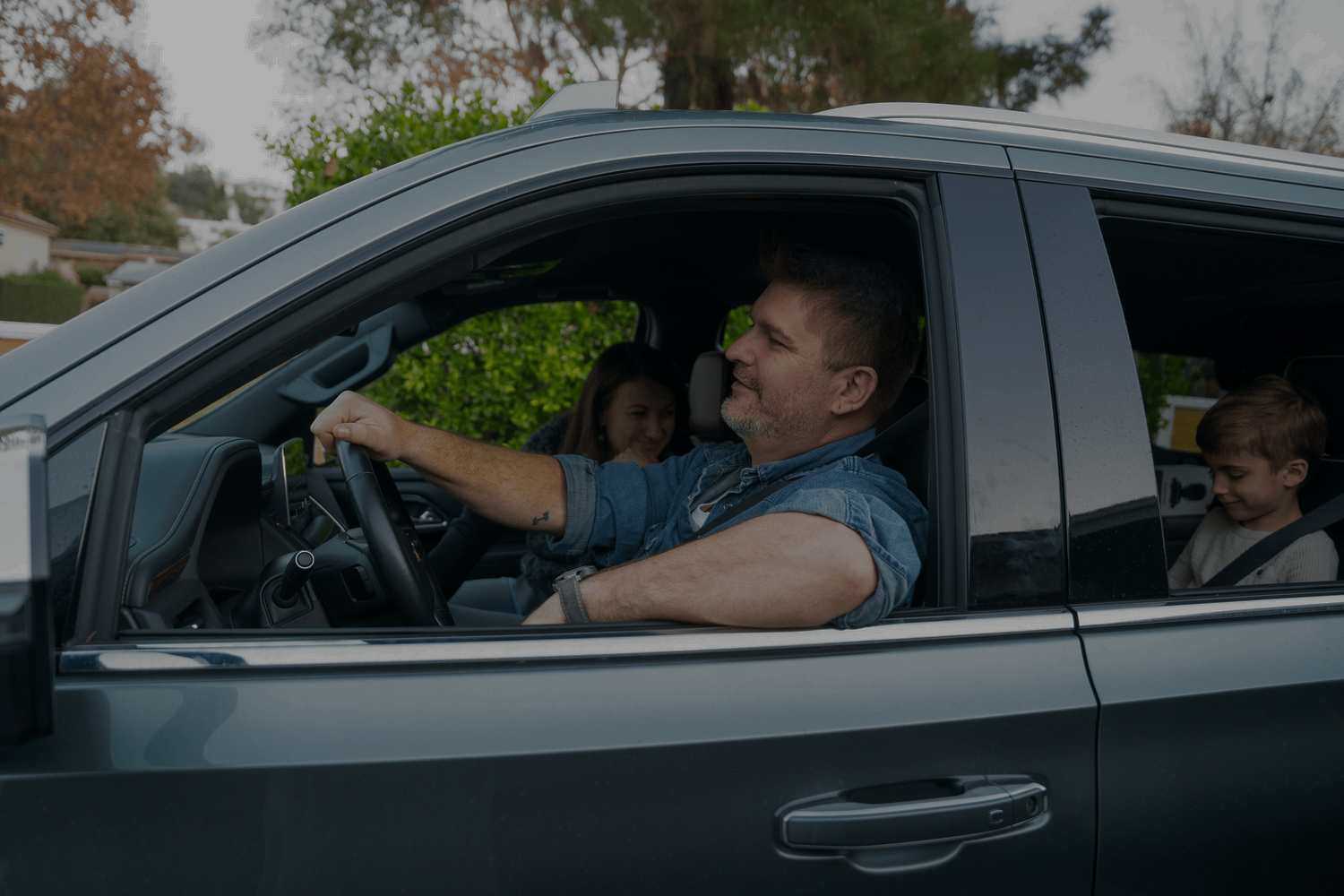 Man driving a car with two passengers inside, smiling.