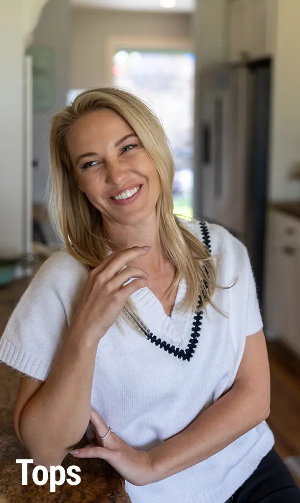 Smiling woman in a white top, sitting in a kitchen.