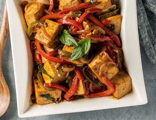 Stir-fried tofu with red peppers and basil in a white dish.