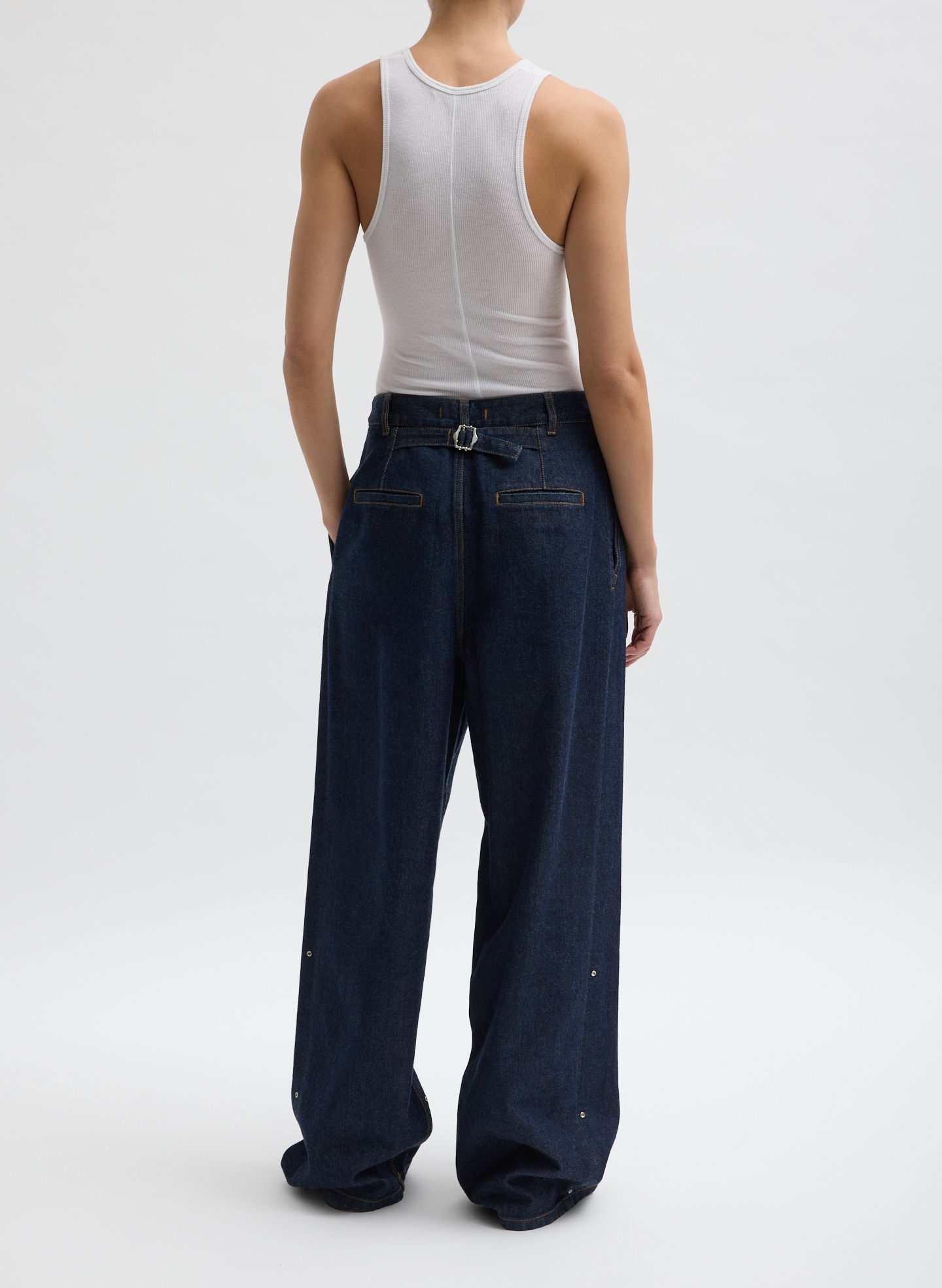 Person wearing a white tank top and baggy blue jeans, viewed from behind.