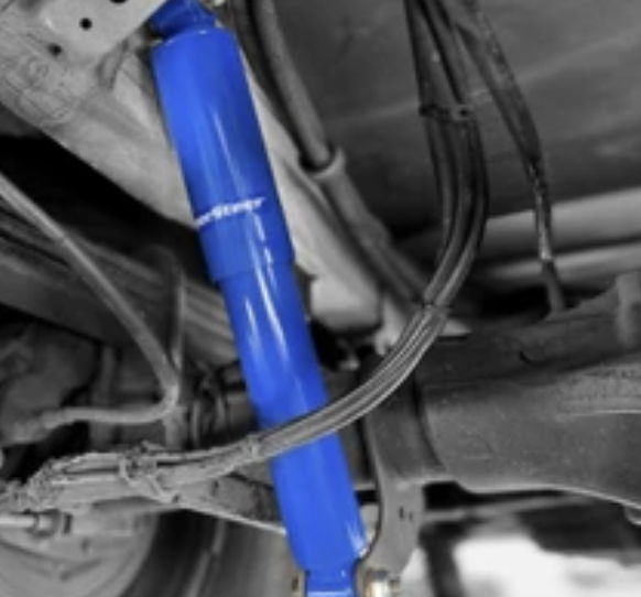 Blue shock absorber mounted under a vehicle, with surrounding components in grayscale.