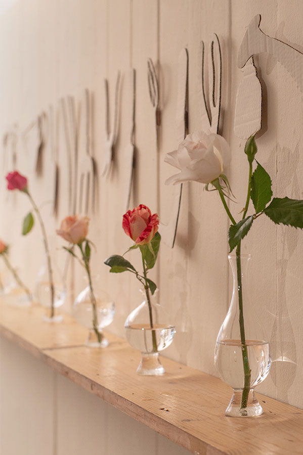 Roses in vases on a shelf with fork decorations on the wall.