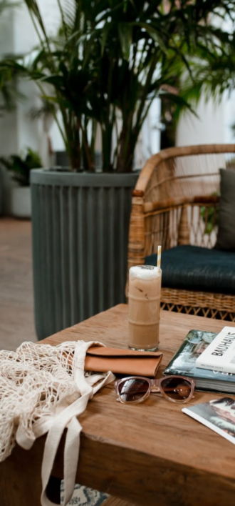 A cozy setting with a drink, sunglasses, and magazines on a wooden table.