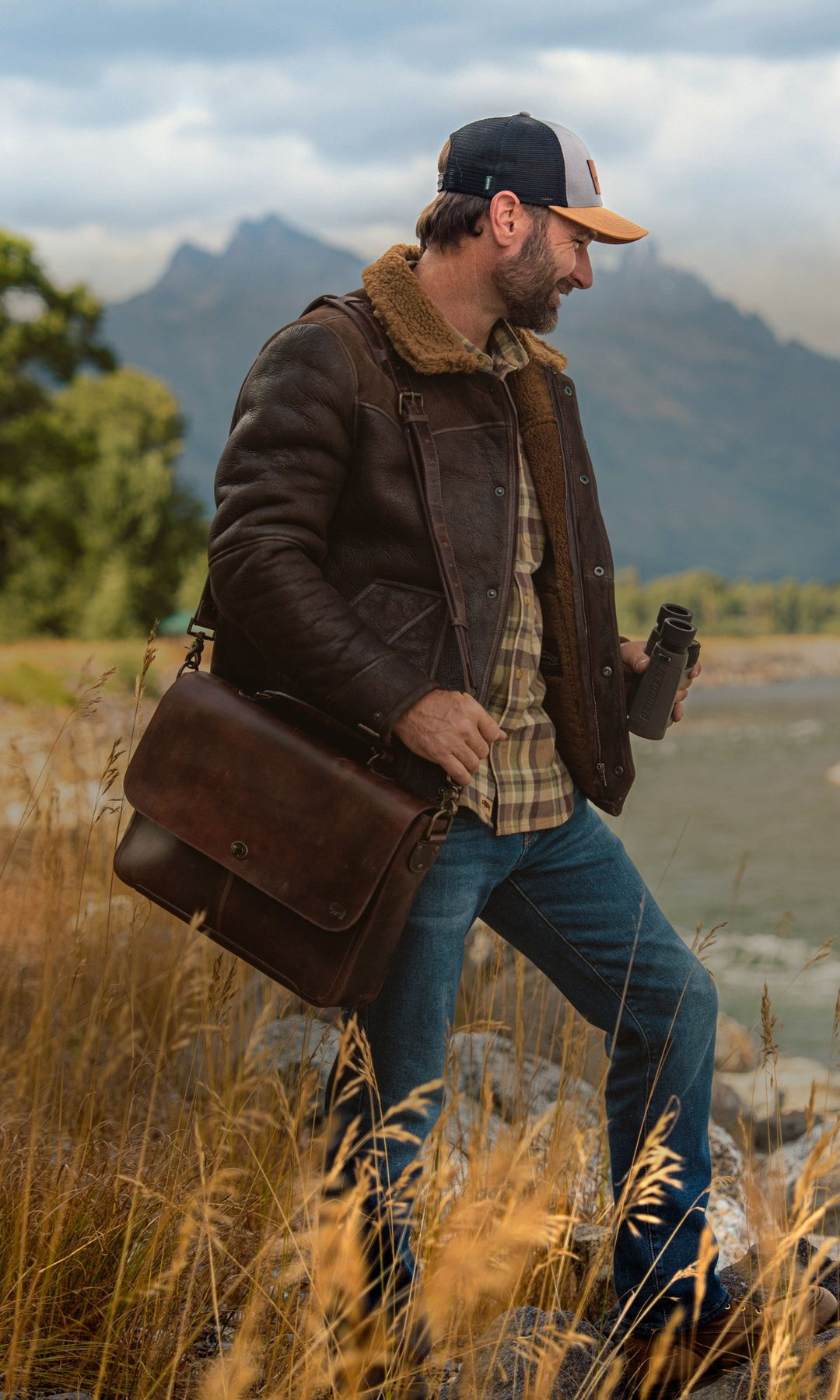 Man in a Buffalo Jackson shearling leather jacket carrying a dark brown leather messenger bag along a mountain river