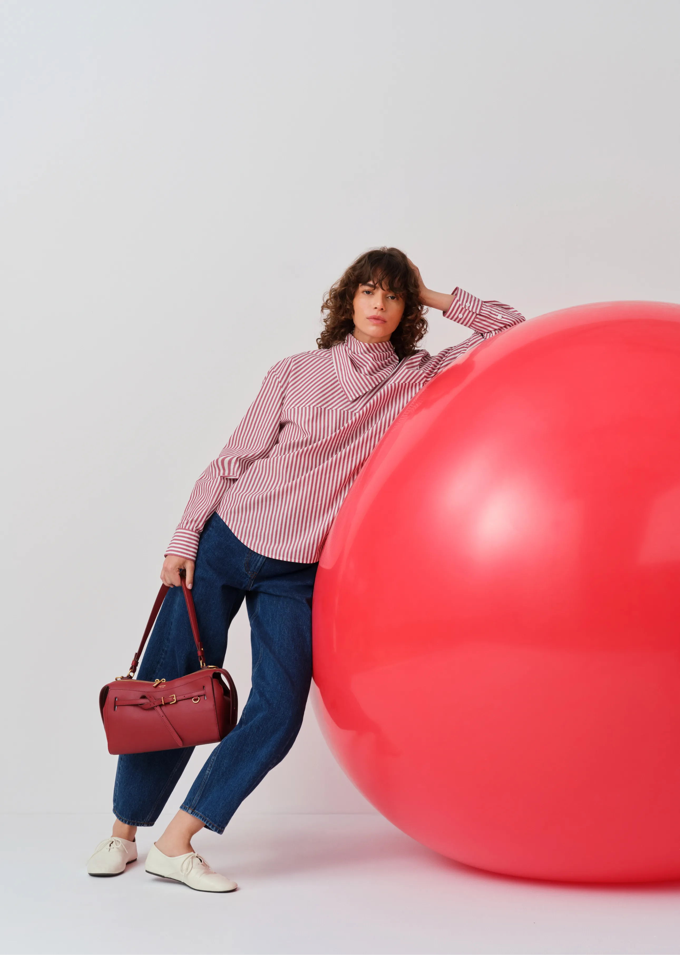 Woman leaning against a large pink sphere, holding a handbag.