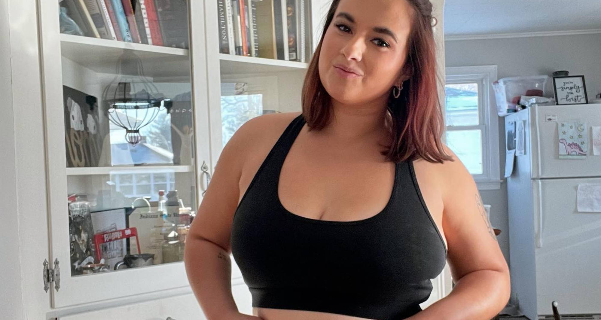 woman smiling wearing a matching black bra and high waisted undies set in front of a white bookshelf