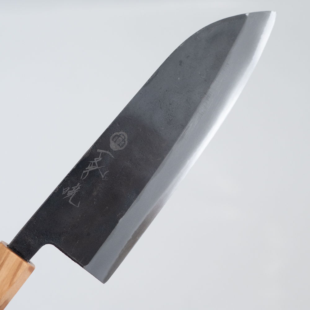 A front facing shot of a santoku knife, with a black rustic finish on the flat of the blade.