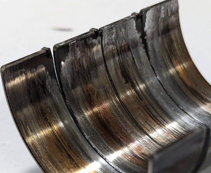 Close-up of worn engine bearing shells showing surface wear and damage.