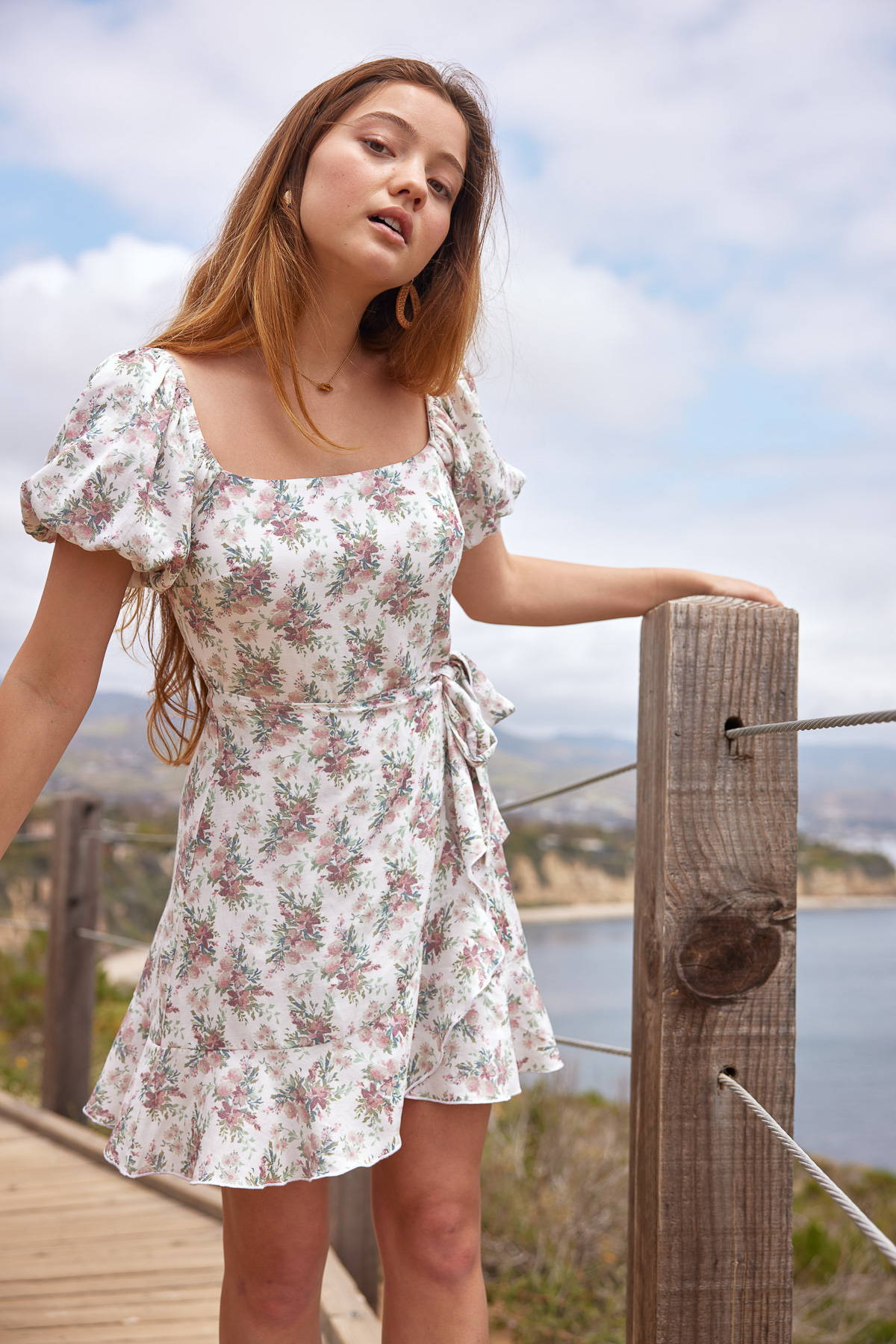Trixxi sun-kissed summer, girl at ocean side beach pier, in floral wrap ruffle puff sleeve dress.