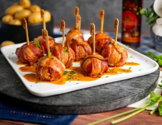 Bacon-wrapped meatballs on a platter with sauce and garnishes.