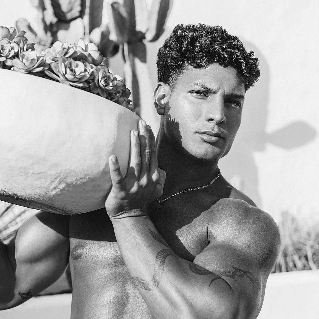 A muscular person carrying a large bowl of plants outdoors.