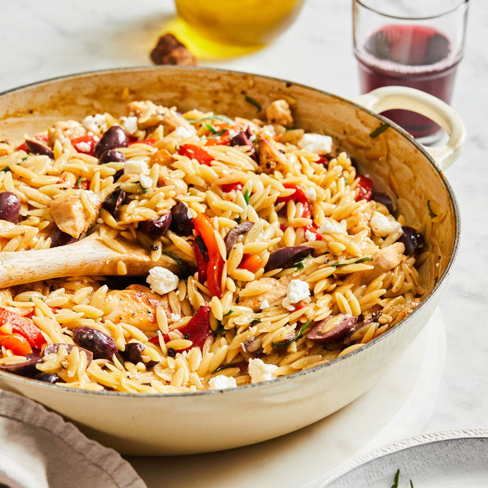 Cooked orzo pasta in a skillet with red peppers, olives and feta cheese