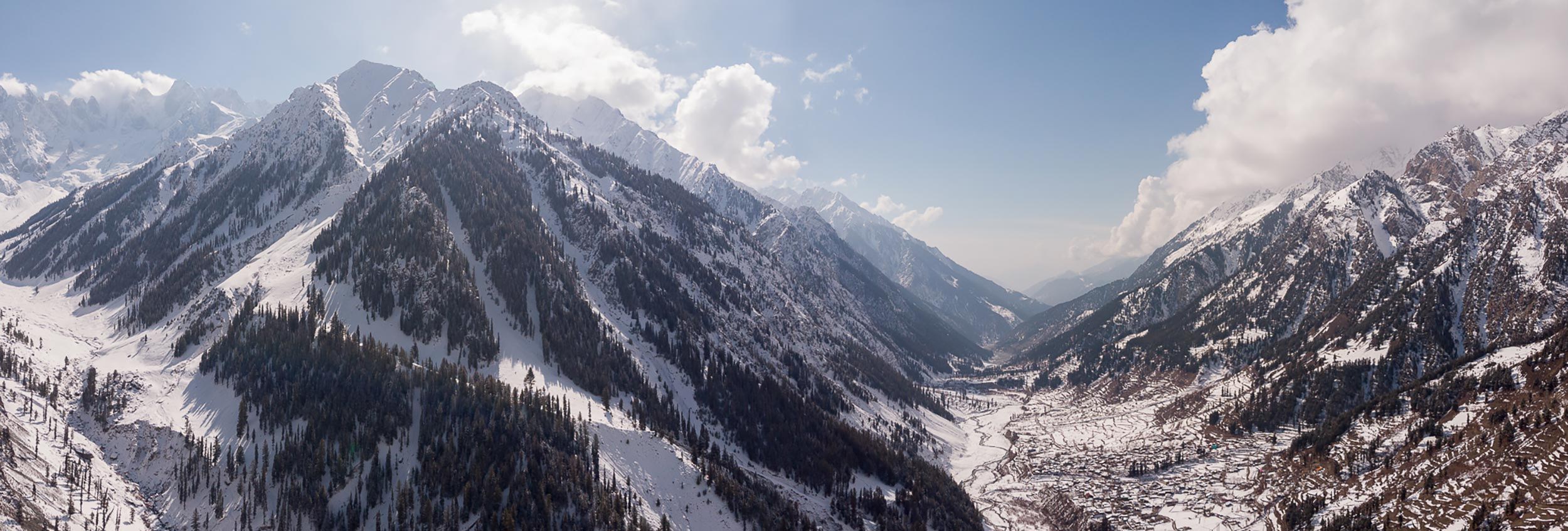 Snow-covered mountains under a clear blue sky with clouds.