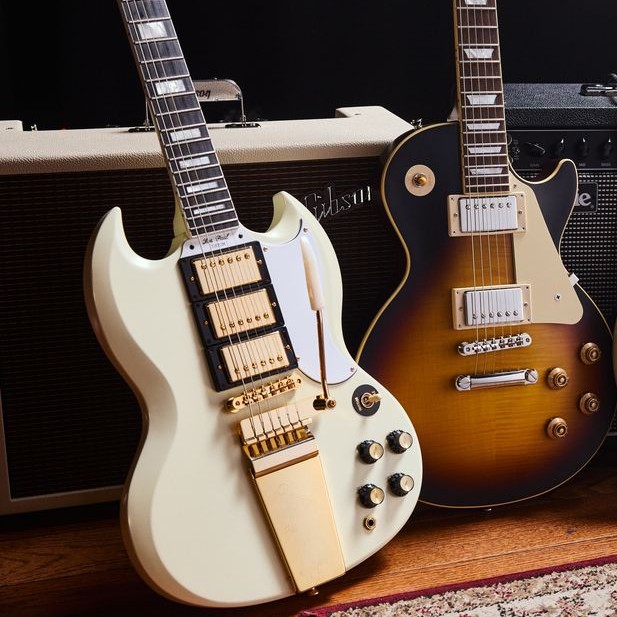 Two electric guitars leaning against an amplifier on a wooden floor.