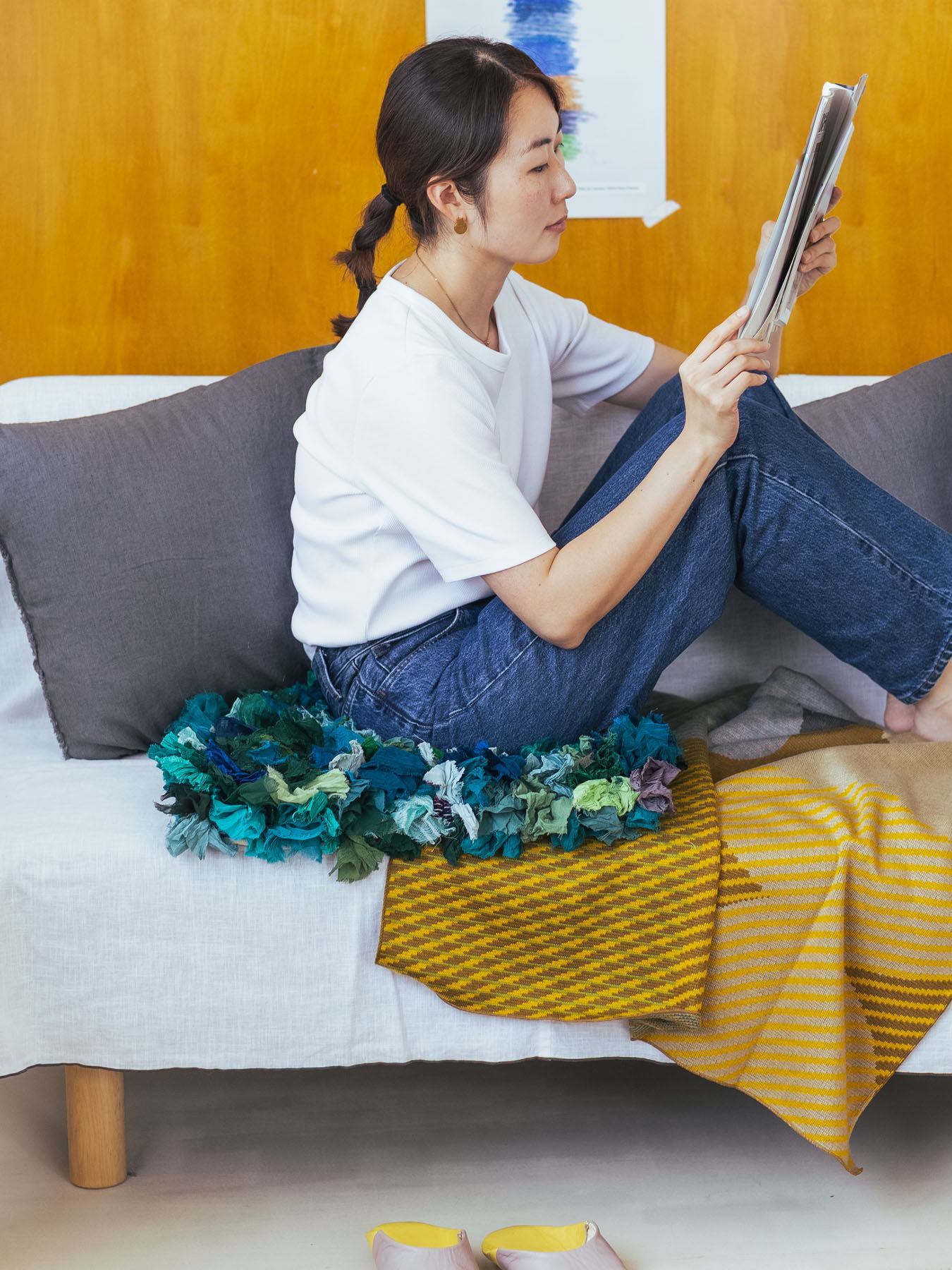 Woman reading a magazine while sitting on a couch with colorful blankets.