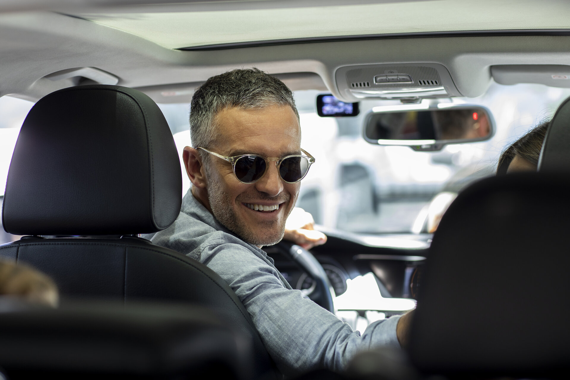 Person wearing sunglasses, smiling while sitting in a car.